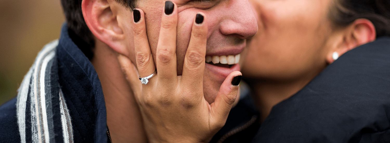 Woman kissing man on cheek with solitaire diamond engagement ring